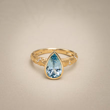 Load image into Gallery viewer, 18k yellow gold ring featuring a pear-shaped aquamarine in a protective bezel setting with a hand-engraved textured band and inset diamonds.
